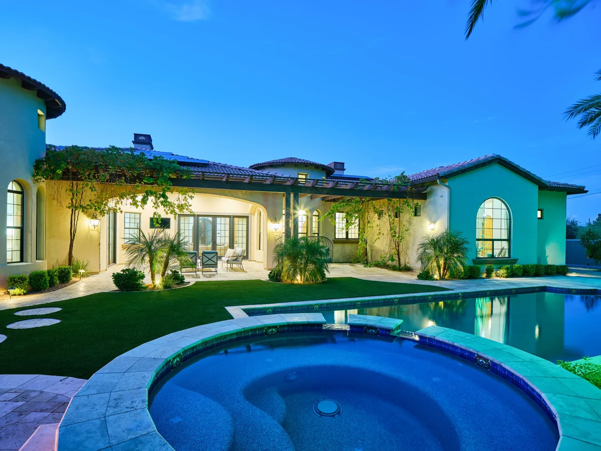 A view of the backyard showcasing the swimming pool, bubbling spa, outdoor seating area, and vibrant landscaping. The scene emphasizes the spa’s inviting presence, surrounded by greenery and architectural elements of the home, evoking luxury and seasonal comfort.