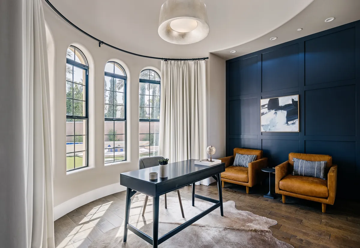 A focused view of a dedicated office space within a bedroom, featuring arched windows that flood the area with natural light, a wooden desk, and elegant leather chairs. The calm, focused atmosphere is perfect for remote work or quiet reflection.