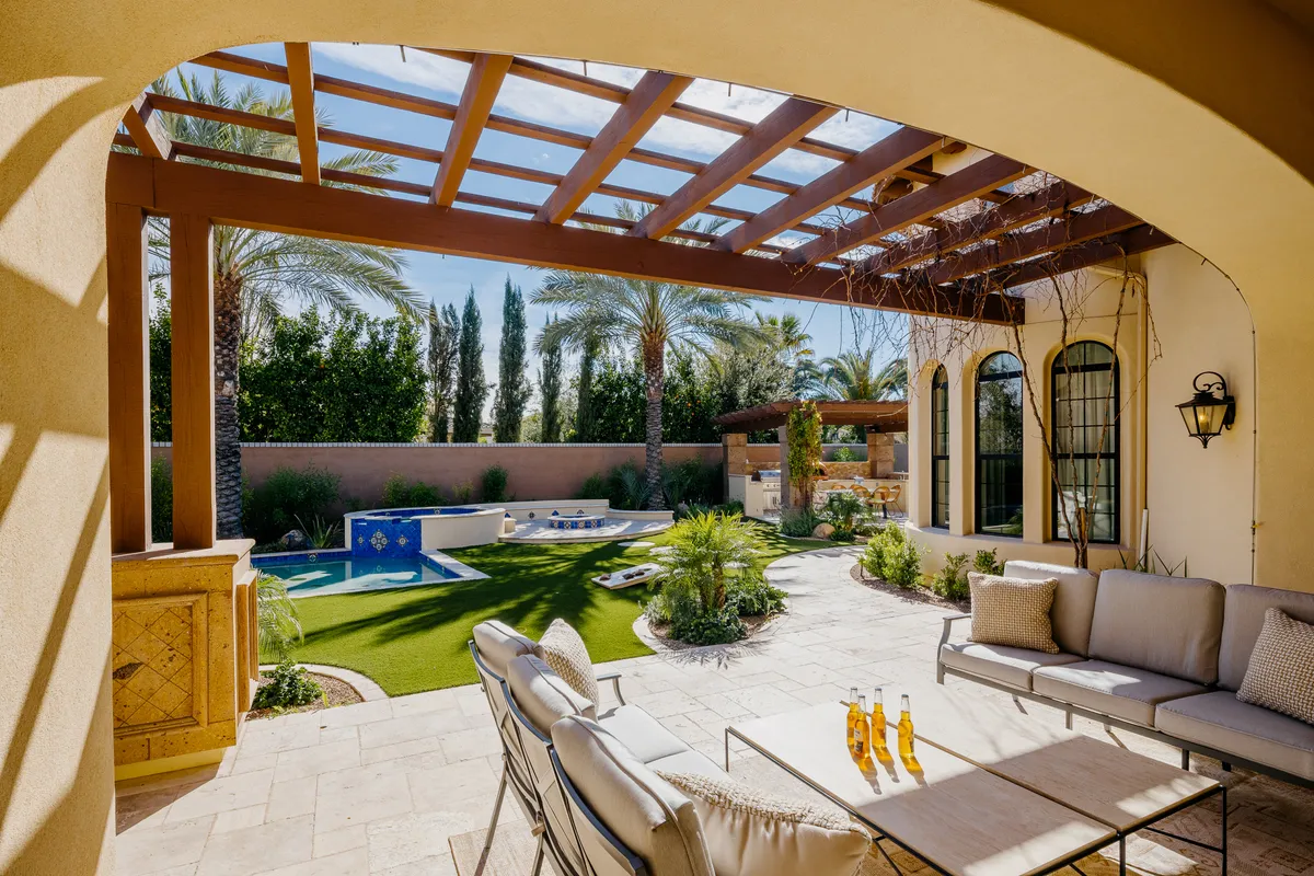 A lively exterior photo of the home's backyard, showcasing the swimming pool, outdoor seating area beneath a pergola, and lush greenery. The scene suggests relaxation and play, ideal for family gatherings, pool time, and outdoor games.
