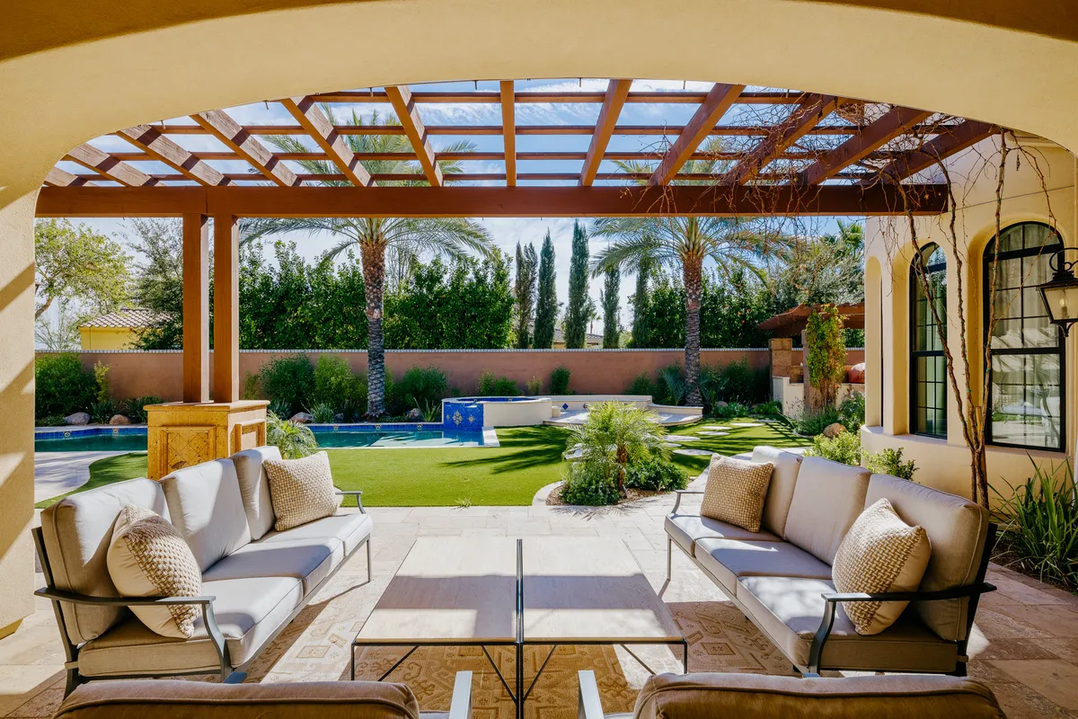 An inviting outdoor seating area sits beside a swimming pool, surrounded by palm trees and a landscaped garden. The tranquil space is ideal for relaxing, socializing, or enjoying a quiet moment outside.
